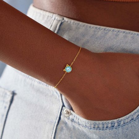 Detailed product view of the cat-themed bracelet, highlighting the polished gold finish and central blue gem.