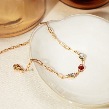 Close-up of a gold paperclip chain bracelet with colorful CZ stones.