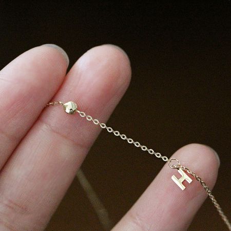 Detailed view of the gold chain and 'H' charm on the sterling silver bracelet.