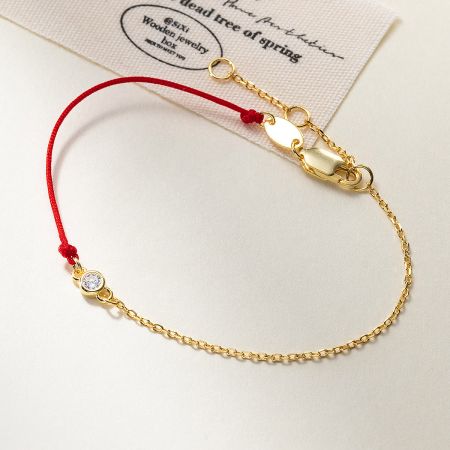 Detailed view of a single 925 silver red string bracelet with a gold chain and cubic zirconia stone.