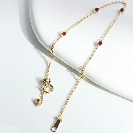 Detailed view of the gold link chain bracelet showcasing the vibrant red gemstones.