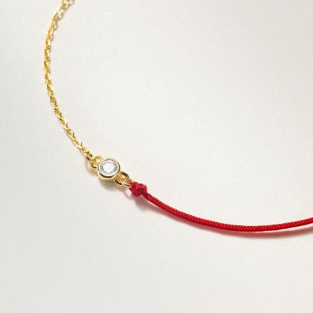 Close-up of the sparkling cubic zirconia charm on the red string and gold chain bracelet.