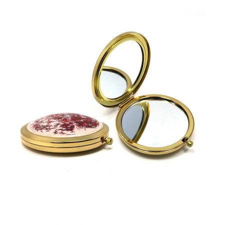 Top view of the gold compact mirror with a decorative lid, featuring a white base with vibrant red and pink glitter specks.