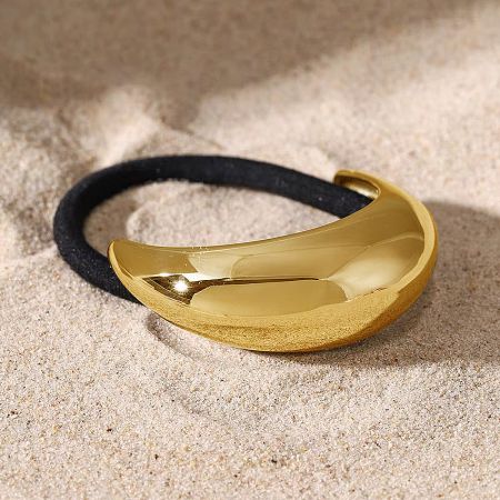 Detailed shot of the gold crescent-shaped hair cuff on a sandy background.