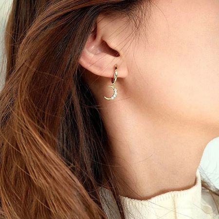 Close-up of the gold crescent moon earring with embedded stones, worn by a model.