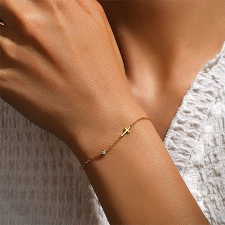 Model wearing the gold cross and cubic zirconia charm bracelet, showcasing its delicate design on the wrist.