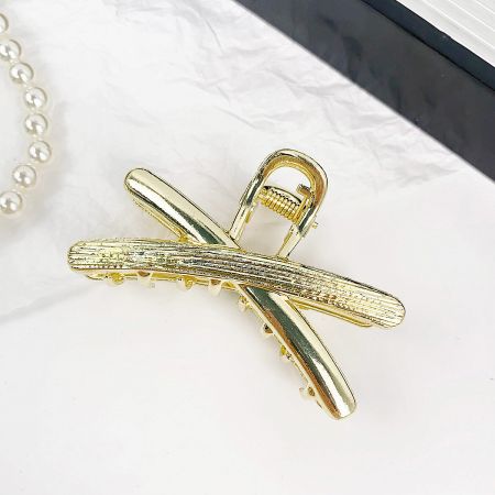 Detailed view of the gold cross-shaped hair clip, highlighting its metallic sheen.