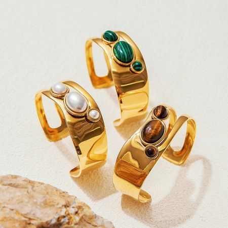 A set of three gold cuff bracelets featuring natural pearl, tiger-eye, and malachite gemstones.