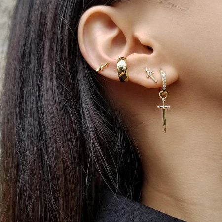 A collection of various gold dagger-themed earrings displayed together.