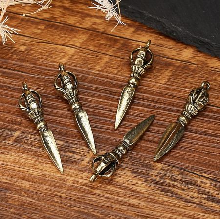 A collection of five custom Tibetan esoteric patriarchal instrument charms in a gold finish, displayed on wood.