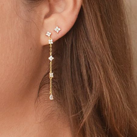 Side view of a gold dangling earring highlighting the flower-shaped settings and brilliant white gemstones.