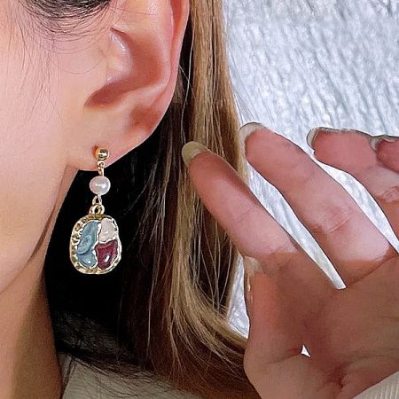Modern gold dangling earring with an oval pendant showcasing a tri-color enamel design.