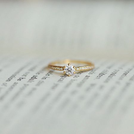 Elegant close-up of the gold-plated solitaire CZ ring resting on a book, highlighting its classic design.