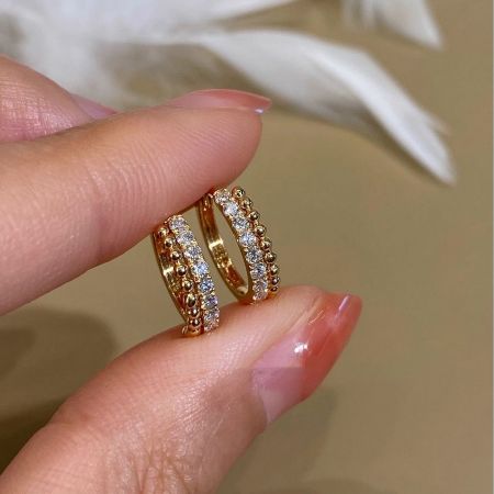A hand holding two 18k gold plated sterling silver huggie hoops to display their intricate CZ bead detailing.