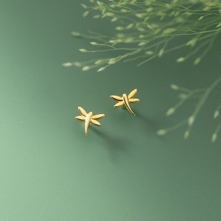 A pair of elegant gold dragonfly stud earrings on a green background.