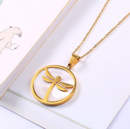 Close-up view of the gold dragonfly pendant necklace, highlighting the detailed craftsmanship and shell background.