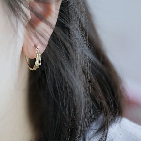 Close-up view of the gold-plated feather leaf hoop earring being worn.