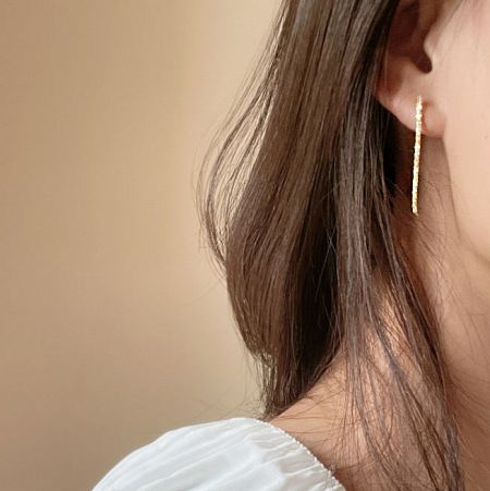 Close-up view of the gold sparkling long earring being worn to show its scale and fit.