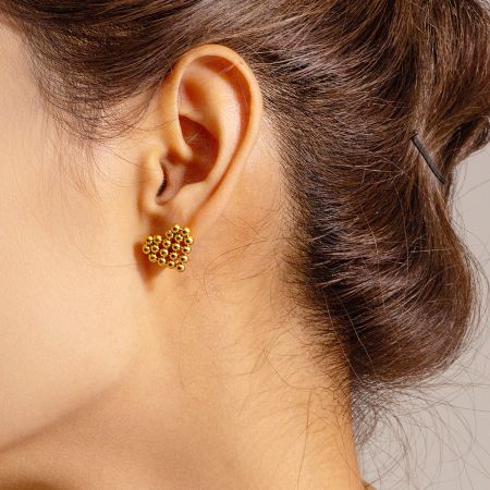 Close-up view of the gold heart shaped stud earring on a model's ear.
