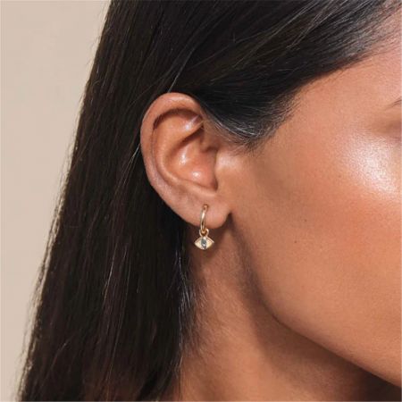 Detailed shot of a gold huggie earring with a diamond-shaped charm and blue gemstone.