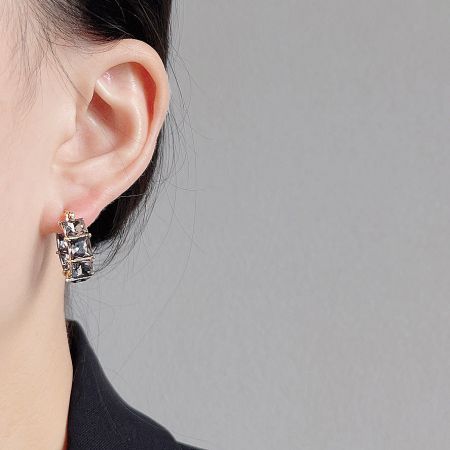 Close-up of a model wearing gold earrings with square gray stones.