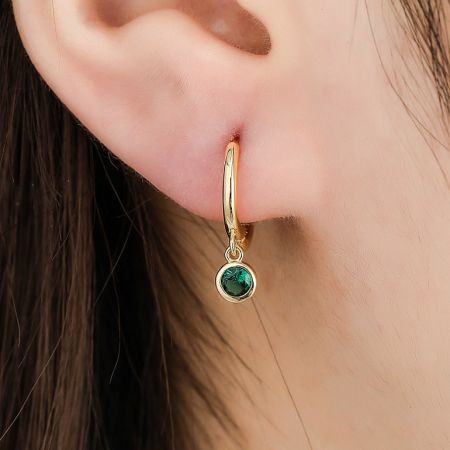 Close-up of the green simulated emerald huggie hoop earring being worn.