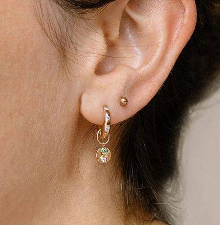 Close-up of a gold hoop earring featuring a vibrant green gemstone charm and a delicate pearl.