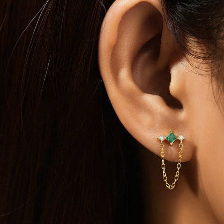Detailed view of a gold tassel earring featuring a vibrant green gemstone and white zircon accents.