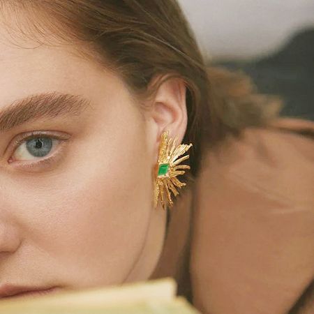 Macro shot of the gold earring, detailing the texture and the central green gemstone.