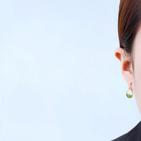 Model wearing a gold earring with a green teardrop-shaped stone, showcasing its elegant drop.