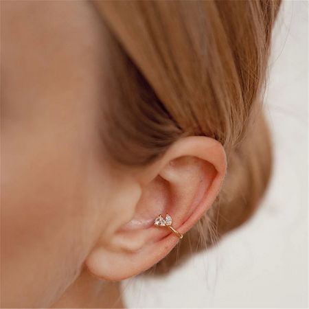 Model wearing a minimalist gold ear cuff with two sparkling clear gemstones.