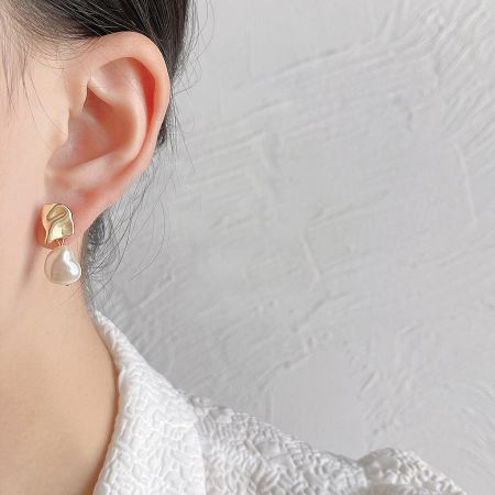 Close-up of a gold earring featuring a large, lustrous white baroque pearl.