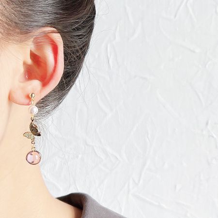 Close-up of a gold drop earring with a pearl, leaf charm, and pink gemstone.