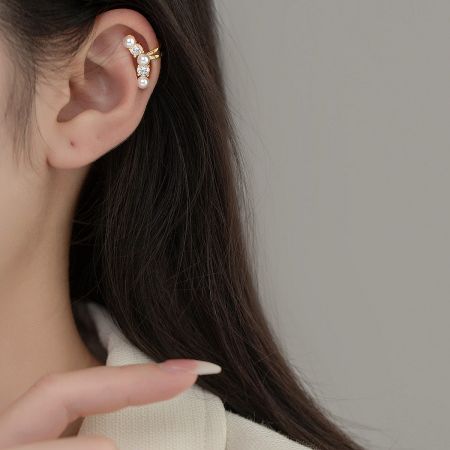 A stylish gold-plated pearl ear cuff with gemstone details, shown as part of a curated ear stack.