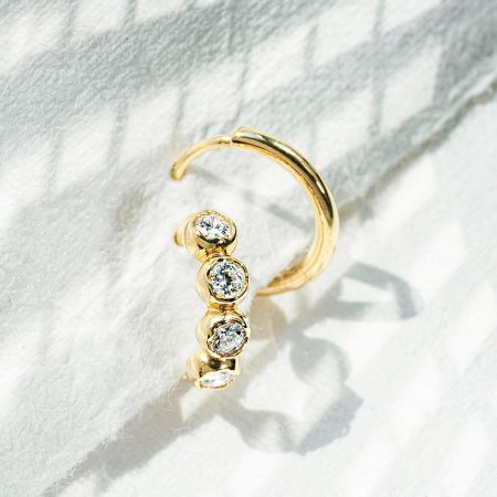 A sterling silver hoop earring with three clear CZ stones on a textured white background.