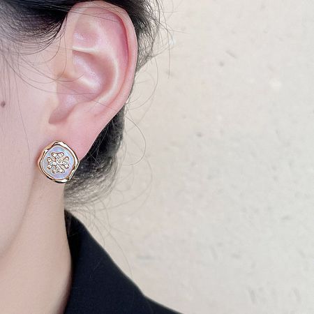 Detailed view of a single gold stud earring with a white and gold floral pattern.