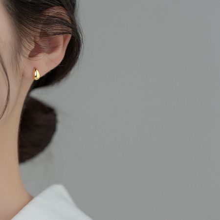 A close-up of a woman wearing the elegant gold water-drop stud earring, highlighting its shine and fit.