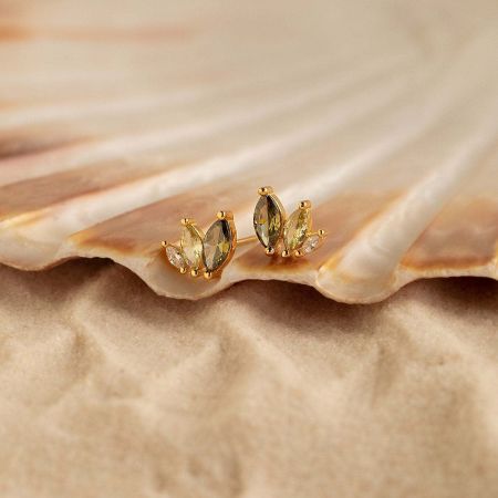 A pair of gold-plated marquise stud earrings with citrine and white gemstones displayed next to a seashell.