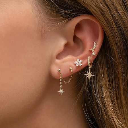 A model wearing a collection of gold earrings, including the star pendant style, to display how they can be layered.