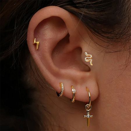 A collection of gold earrings, including the snake stud, styled in multiple ear piercings.