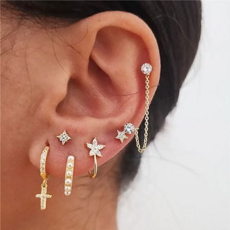 A close-up of multiple gold earrings worn on an ear, including the star stud.