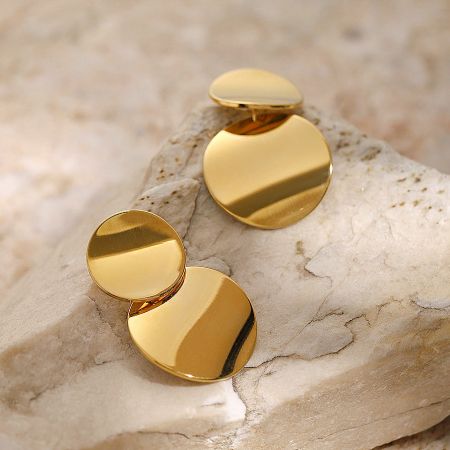 The geometric round disc earrings displayed elegantly on a textured beige stone.