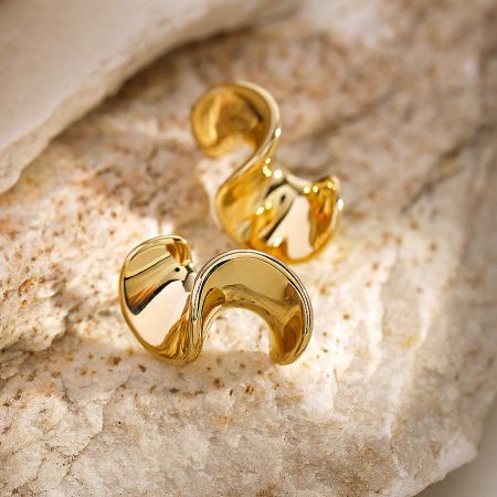 Detailed view of the gold wavy stud earrings on a textured stone surface.