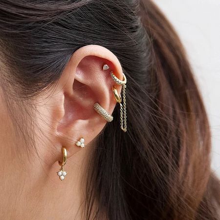 Close-up of gold and silver zircon ear cuffs worn on an ear for a fashionable, layered style.