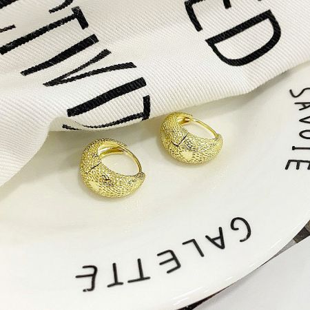 Lifestyle shot of the gold bag-shape hoop earrings resting on a white ceramic dish.