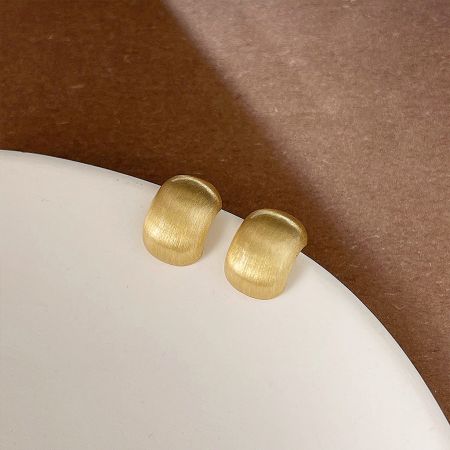 A pair of gold French metal bead design stud earrings on a display stand.