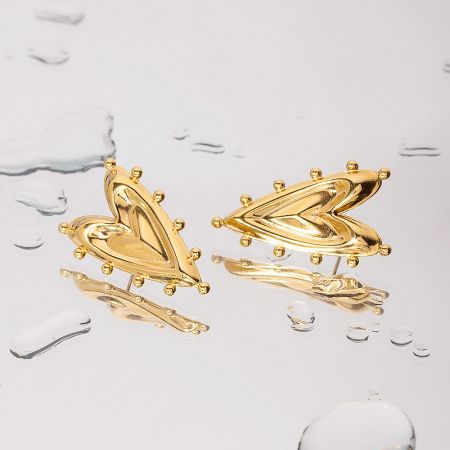 Product shot of the abstract gold heart earrings on a white surface with water droplets, highlighting their reflective finish.