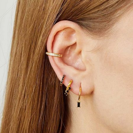 Close-up view of the gold huggie earrings with black stones styled on an ear.