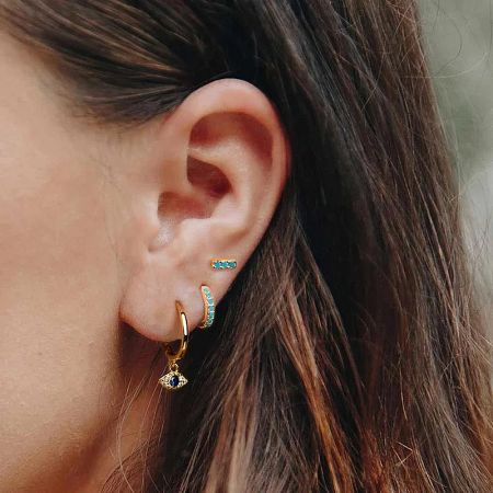 Side profile of a model wearing the gold evil eye earrings with blue gemstones.