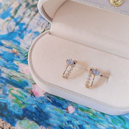 A pair of dual-layer stud earrings with blue gemstones elegantly presented in a white jewelry box.
